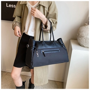 Detail of a black large capacity leather tote bag with side buckles and zipper pockets