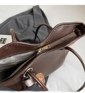 Detail of smooth golden metal zipper and interior pocket on dark brown PU leather tote