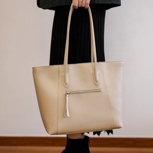 Detail of beige leather tote bag featuring a metal zipper pocket and elegant tassel