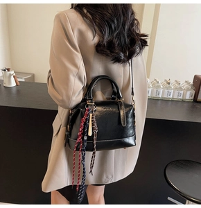 Dettaglio di una borsa Boston nera in pelle con ciondolo intrecciato e tracolla