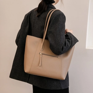Brown leather tote bag featuring sleek long handles and front zipper on model