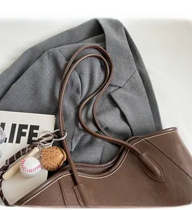 Detail of dark brown leather tote bag with vintage baseball charms on a grey blazer