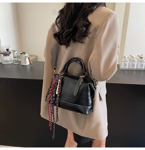 Dettaglio borsa Boston in pelle lucida nera con nappe intrecciate e tracolla sottile