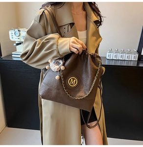 Detail of brown leather bucket bag with gold M logo, chain, and cute plush charm pendant