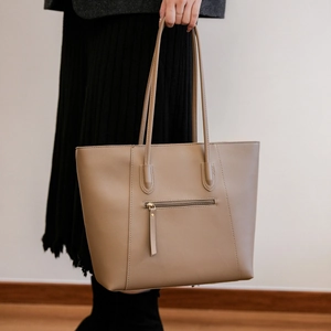 Detail of khaki leather tote bag featuring a front zipper pocket and long puller detail