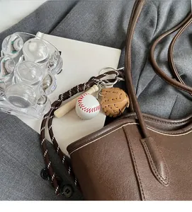 Detail of baseball glove, bat and ball keychain charm hanging on brown PU leather bag