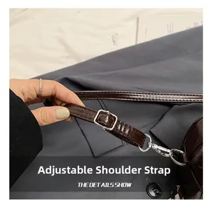 Détail de la bandoulière réglable avec boucle argentée sur le sac polochon marron foncé