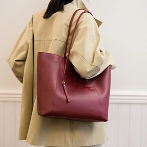 Detail of burgundy large tote bag with a rear zipper pocket on a khaki trench coat