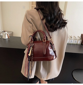 Dettaglio della borsa Boston in pelle bordeaux con cuciture a contrasto e ciondolo