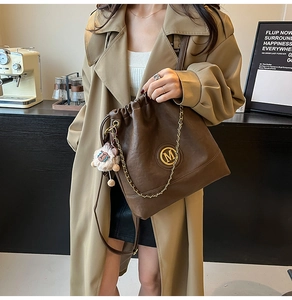 Brown leather bucket bag with gold M logo, chain detail and sheep plush keychain