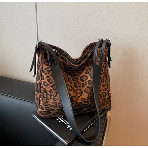 Detail of leopard print tote bag with black leather straps on a dark sofa background