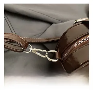 Détail du sac en cuir verni marron foncé avec crochet métallique argenté et fermeture éclair