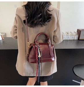 Borsa Boston in pelle bordeaux indossata da modella con ciondolo intrecciato tricolore
