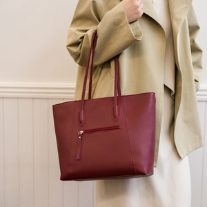Detail of burgundy leather tote bag featuring a front zipper pocket worn with a trench coat