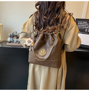 Detail of coffee brown leather bucket bag with gold M logo and plush lamb charm accessory