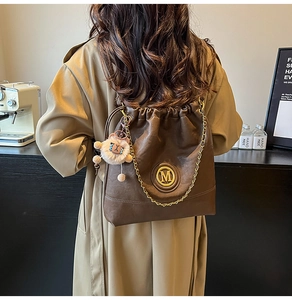 Detail view of coffee leather drawstring backpack with gold chain and plush charm pendant