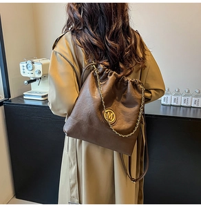 Detail of dark brown leather bag with metallic M logo and chain decoration