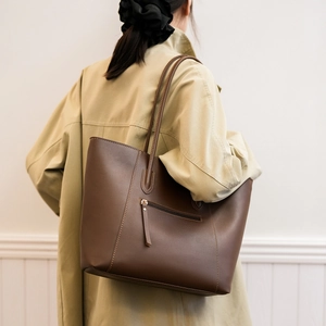 Detail of dark brown leather tote bag with zip pocket shown on a model in a trench coat