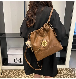Detail view of brown drawstring bucket bag with gold chain and plush charm accessory