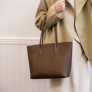 Detail of a large dark brown tote bag styled with a trench coat for a classic commuter look