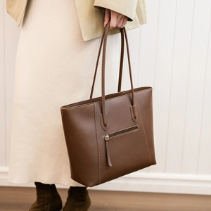 Detailed close-up of stitching and front zipper pocket on dark brown leather tote bag