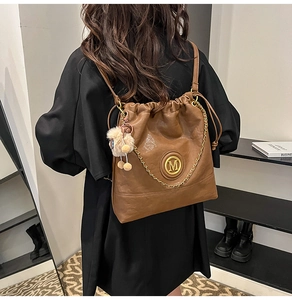 Detail of brown leather backpack with gold chain trim and plush ball accessory