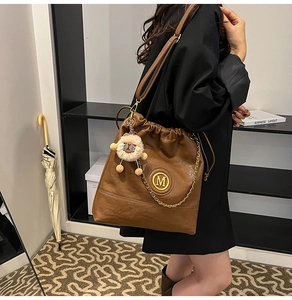 Detail of brown leather bucket bag with gold M-logo, chain, and plush charm