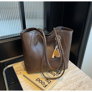 Detail view of brown matte leather tote bag with creative baseball glove charm on side