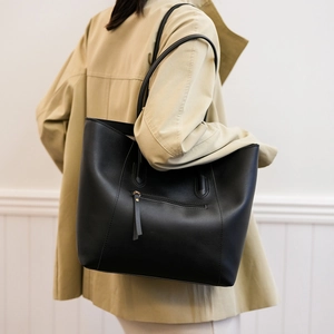 Detail of a large black leather tote bag featuring an exterior zipper pocket with long tassels