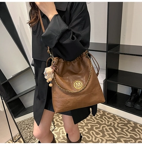 Detail of brown leather bucket bag with gold M logo, chain strap and plush keychain