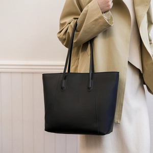 Detailed view of a black leather tote bag worn with a khaki coat for size reference