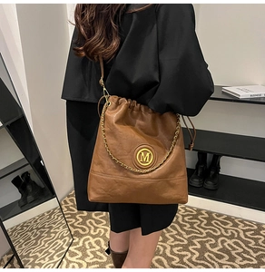 Detail of a brown vintage leather bucket bag with a golden M logo and chain strap