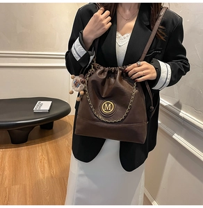 Detail view of brown PU leather bucket bag with golden metal M logo and plush charm