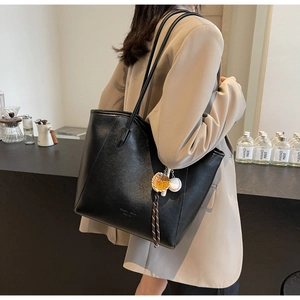 Detail of black leather tote bag with embossed logo and sporty charm accessory