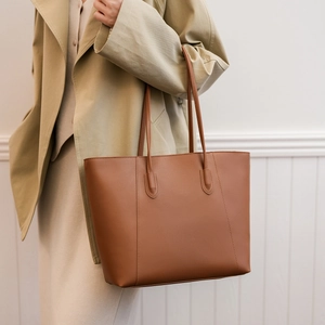 Detail of a large brown leather tote bag with vertical stitching shown on model