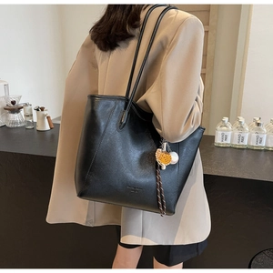 Detail of black tote bag with slender straps and baseball charm in lifestyle setting