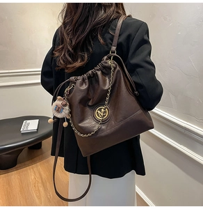 Close-up of brown leather bucket bag with gold chain and M logo worn by model