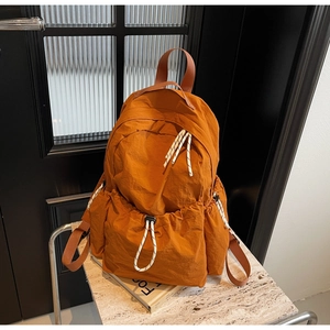 Détail d'un sac à dos orange en nylon avec cordon rayé sur une surface en pierre