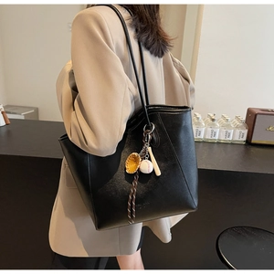 Detail of black tote bag with textured lychee grain leather and sporty baseball pendants
