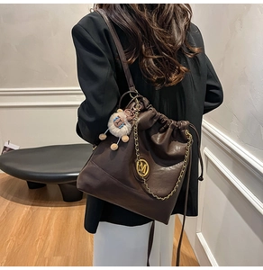Detail of dark brown leather bucket bag with gold M logo on a model in a black blazer