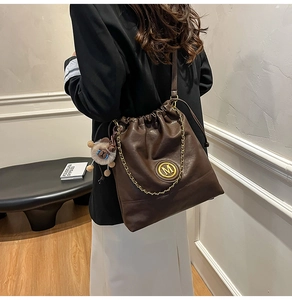 Detail view of large dark brown leather tote bag with gold M logo and chain decoration