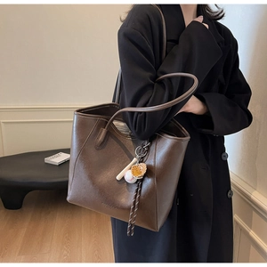 Detail of a large dark brown leather tote bag with a baseball themed keychain accessory