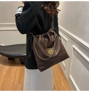 Detail view of deep brown bucket bag with gold M logo and elegant chain strap on a model