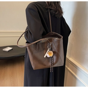 Close-up of a large brown tote bag featuring a decorative baseball pendant with bat and glove