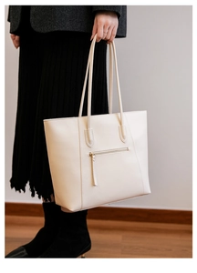 Detail of a large beige leather tote bag with front zipper pocket and long shoulder straps