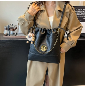 Detail of black leather drawstring bag with metal M logo and plush sheep charm accessory