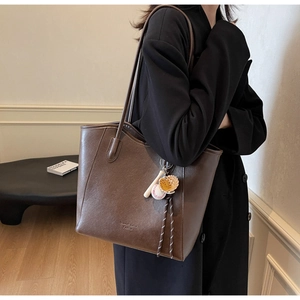 Detail of dark brown leather tote bag with creative baseball charm and litchi texture