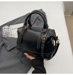 Dettaglio borsa Boston in pelle nera con cuciture bianche su una giacca grigia