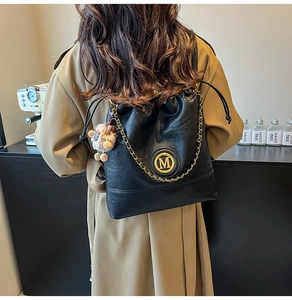 Detail of black drawstring backpack with gold M logo, chain, and plush bear charm