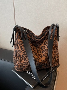 Stylish large leopard print hobo shoulder bag with black leather strap on a decorative book